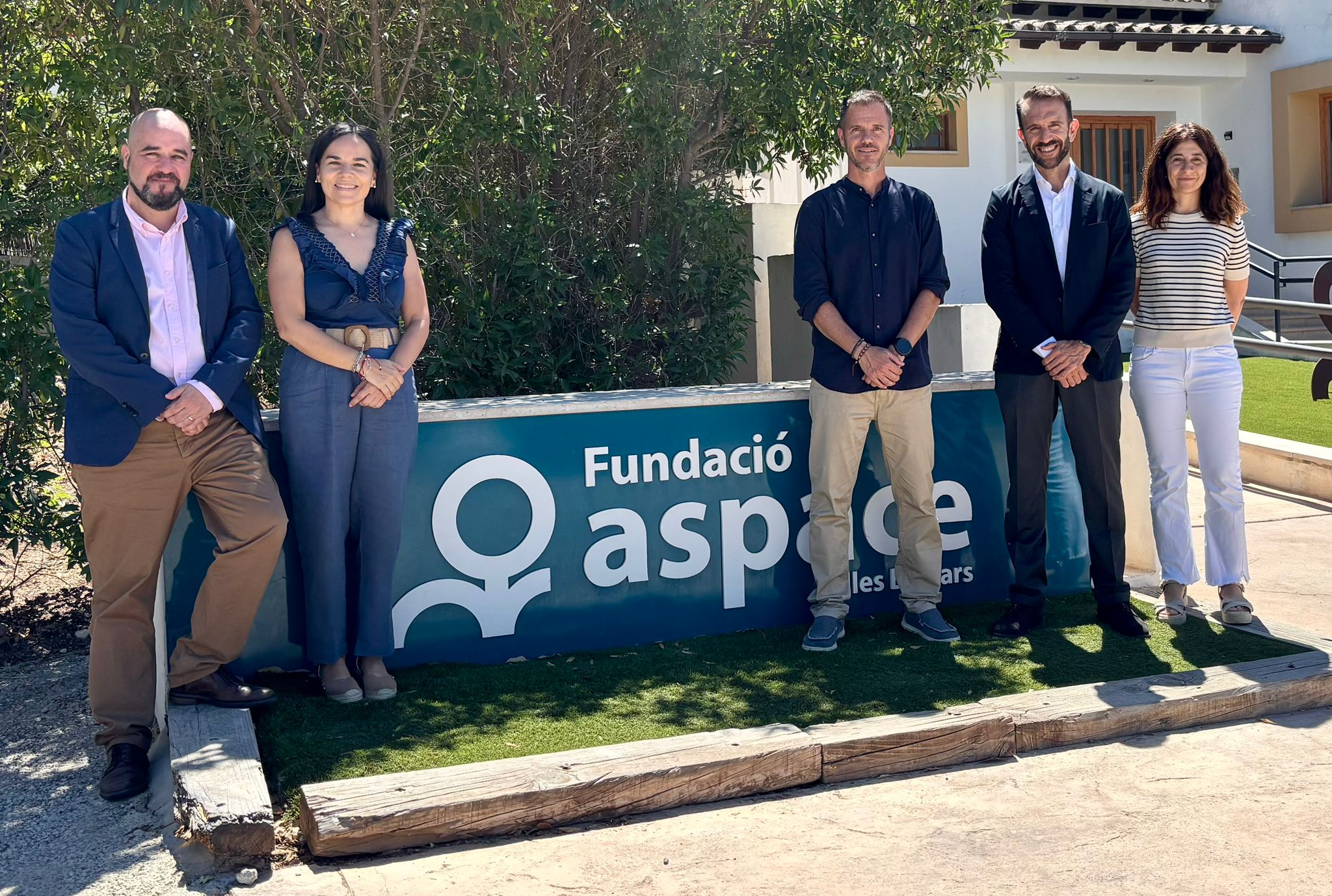 Grupo de cinco personas posando frente al cartel de la Fundación ASPACE en Palma de Mallorca durante una visita institucional relacionada con un proyecto social.