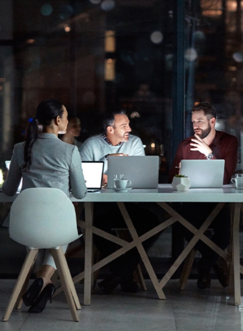 Reunión de trabajo mujer ejecutiva con dos compañeros, usando sus portátiles a última hora del día