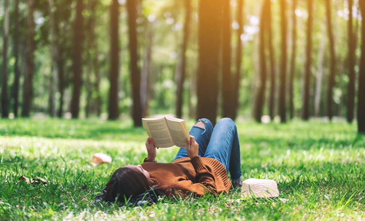 Una mujer tumbada leyendo en el suelo de un bosque